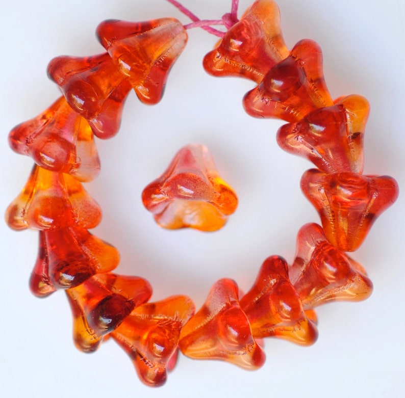 Puede incluir: Una hebra de cuentas de vidrio naranja en forma de flor. Las cuentas son transl&uacute;cidas y tienen un ligero brillo.