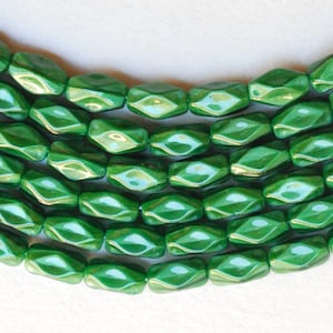 May include: A strand of green glass beads with a faceted, elongated, and slightly curved shape.