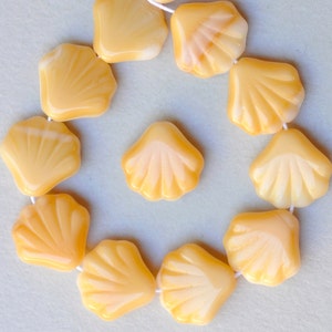 May include: A strand of yellow glass beads shaped like seashells. The beads are strung together with white thread.