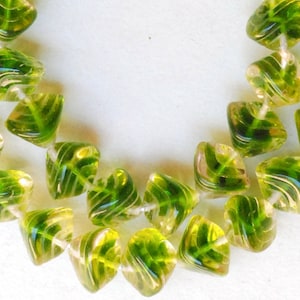May include: A strand of green and clear glass beads with a leaf design. The beads are faceted and have a swirl pattern.