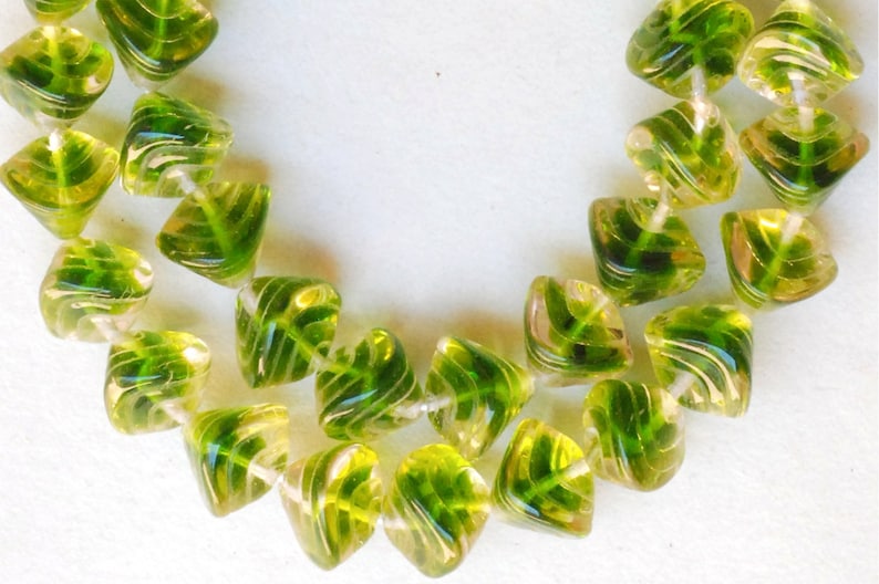 May include: A strand of green and clear glass beads with a leaf design. The beads are faceted and have a swirl pattern.