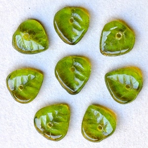 May include: Eight green glass leaf-shaped beads with a hole in the center of each bead.