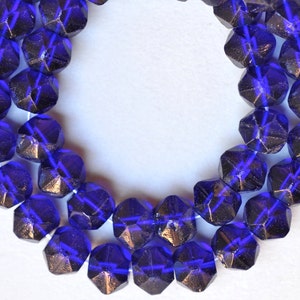 May include: A strand of dark blue faceted glass beads. The beads have a metallic sheen and are strung on a clear thread.