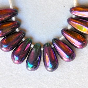 May include: A strand of iridescent teardrop-shaped beads in shades of purple, green, and gold. The beads are strung on a white cord.