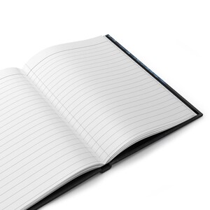 May include: Open notebook with lined pages. The notebook has a black cover and a white interior with gray lines. The pages are open, revealing the lined paper. The notebook is on a white background.