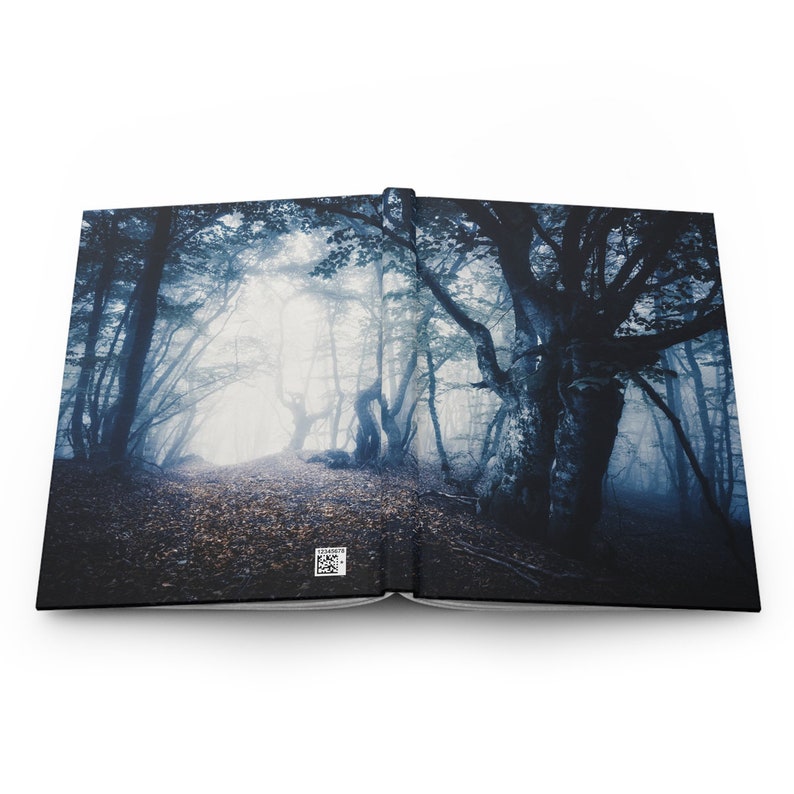 May include: Hardcover journal featuring a misty forest scene. The cover displays a path winding through a dark, atmospheric forest with tall trees and a foggy backdrop. The journal is open, revealing the interior pages.
