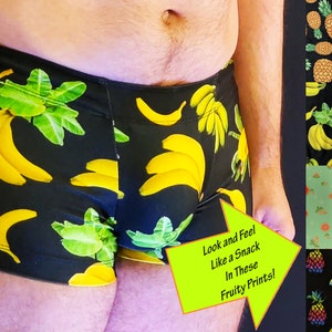 Op de afbeelding: Zwarte boxershorts met een gele banaan en groene bladeren print. De tekst "Look and Feel Like a Snack In These Fruity Prints!" staat op een gele pijl die naar rechts wijst.