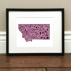 May include: A framed print of a burgundy-colored map of Montana with the names of cities and towns, including "Missoula", "Helena", "Great Falls", "Butte", "Bozeman", and "Billings".