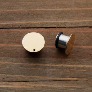 May include: A pair of gold-colored ear gauges, one is a flat disc and the other is a cylindrical plug with a flat disc on one end.