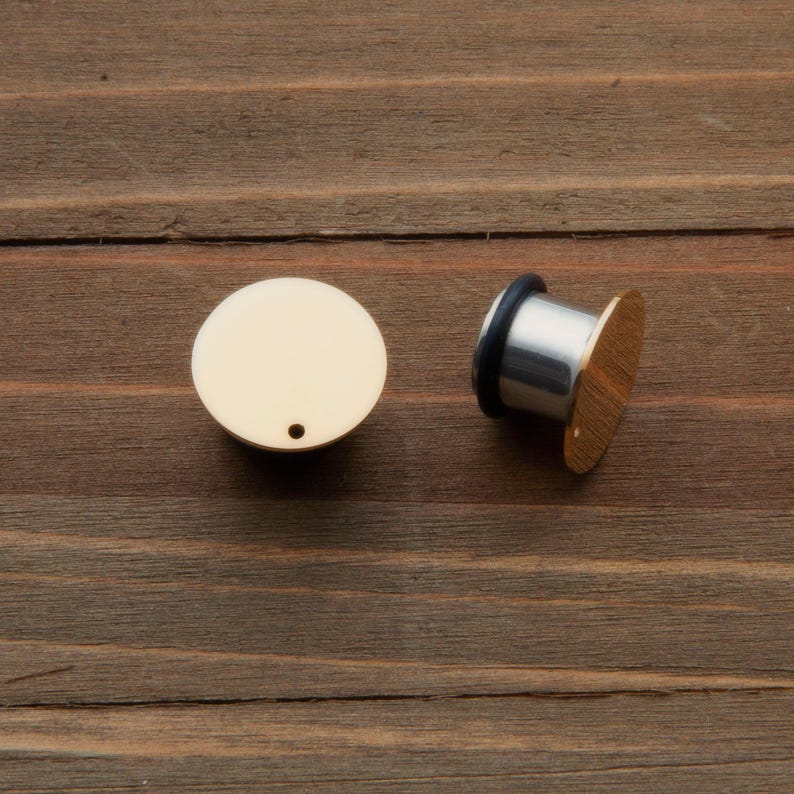May include: A pair of gold-colored ear gauges, one is a flat disc and the other is a cylindrical plug with a flat disc on one end.
