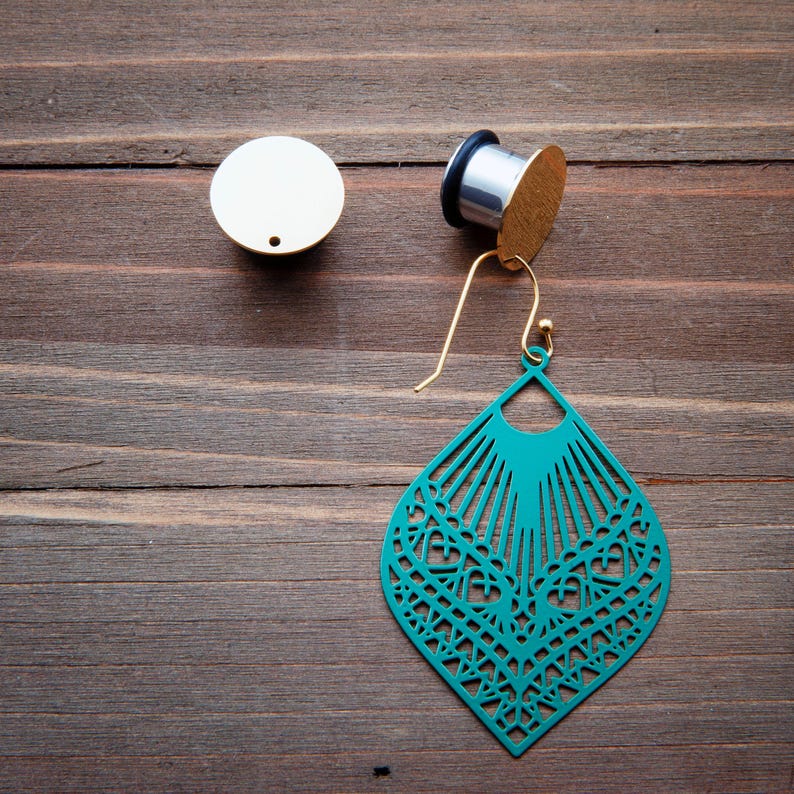 May include: A pair of teal blue earrings with a delicate, intricate design. The earrings are made of metal and have a gold-tone finish. The earrings are hanging from a gold-tone hook.