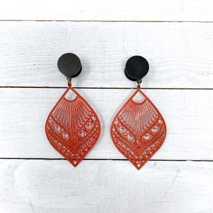 May include: A pair of red filigree earrings with black metal accents. The earrings are in the shape of a teardrop and have a delicate, intricate design.