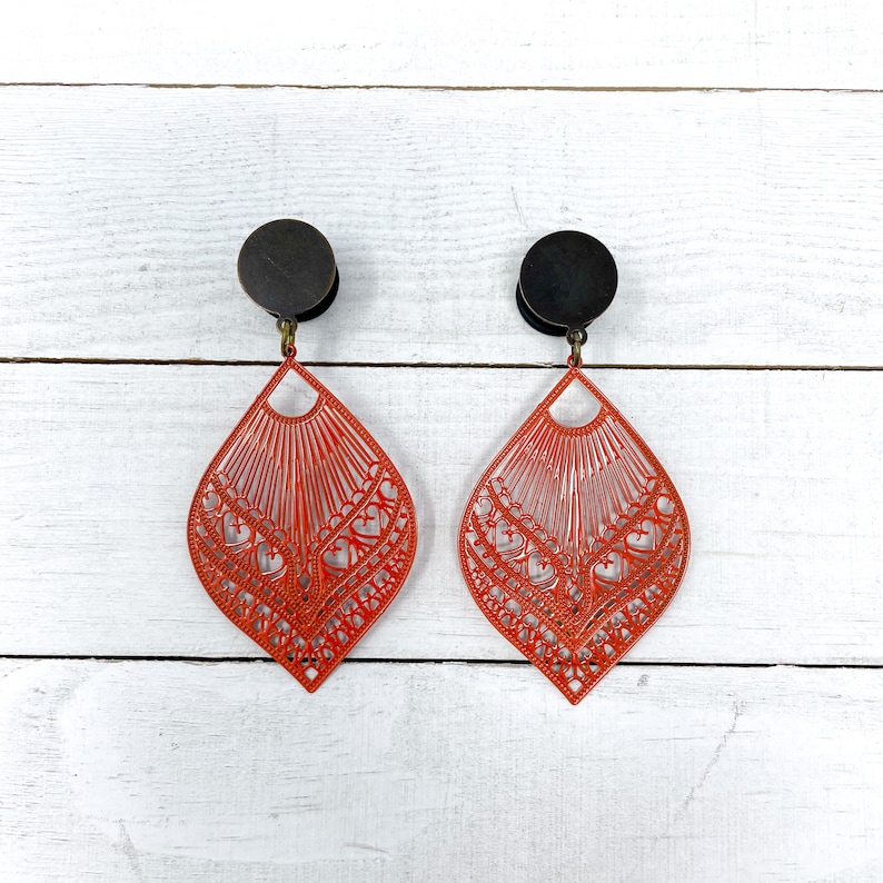 May include: A pair of red filigree earrings with black metal accents. The earrings are in the shape of a teardrop and have a delicate, intricate design.