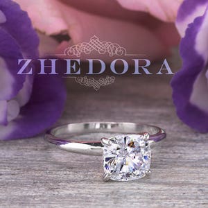 May include: A silver engagement ring with a round, clear diamond set in a simple band. The ring is surrounded by pink and purple flowers.