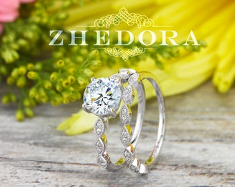 May include: A silver engagement ring set with a large, round, clear centre stone and a delicate band of smaller stones. The ring is set against a background of pink and yellow flowers.