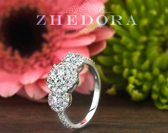 May include: A silver ring with three round diamonds set in a prong setting. The ring is surrounded by pink and green flowers.