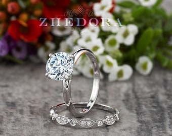 May include: A silver engagement ring set with a large, round, clear diamond. The ring is surrounded by white and pink flowers.