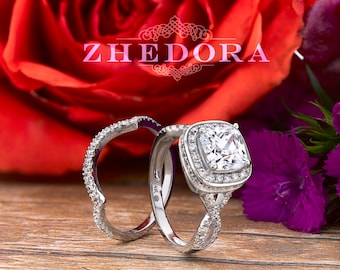 May include: A silver engagement ring set with a large, square-cut diamond surrounded by smaller diamonds. The ring is set on a twisted band. The ring is surrounded by red and purple flowers.