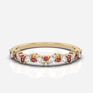 Può includere: Un anello a fascia d'oro con una fila di diamanti a forma di marquise e pietre preziose rosse.