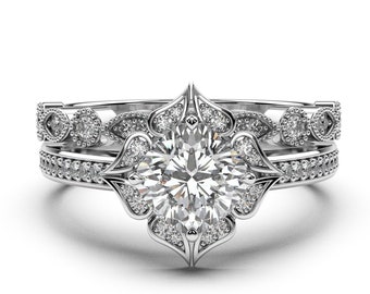 May include: A silver engagement ring set with a large round centre stone surrounded by smaller stones. The ring has a delicate floral design and is set on a band with a matching band.