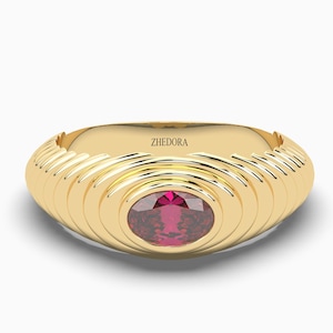 May include: A gold ring with a red gemstone set in a circular design. The ring has a textured band with concentric circles.