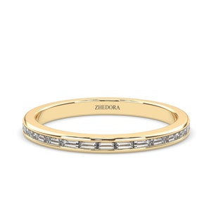 Könnte beinhalten: Ein dünner Goldring mit einer Reihe kleiner, rechteckiger Diamanten, die in einer Kanalfassung gefasst sind. Der Ring ist mit dem Wort "ZHEDORA" beschriftet.