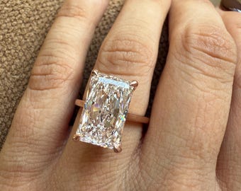 Può includere: Un anello in oro rosa con un grande diamante a taglio rettangolare. Il diamante è trasparente e sfaccettato, riflettendo la luce. L'anello è montato su una fascia delicata, che mette in risalto la brillantezza del diamante.