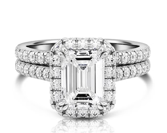 May include: A diamond engagement ring set with an emerald-cut center stone, surrounded by a halo of smaller diamonds. The band is also encrusted with diamonds, creating a sparkling, elegant look. The ring is set in a silver metal.
