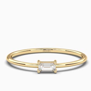 Puede incluir: Un delicado anillo de banda de oro con una pequeña piedra preciosa rectangular transparente engastada en el centro. El anillo está grabado con la palabra "ZHEDORA".