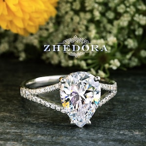 May include: A pear-shaped diamond engagement ring with a split shank and pave diamonds. The ring is set in white gold and features a large, sparkling diamond.