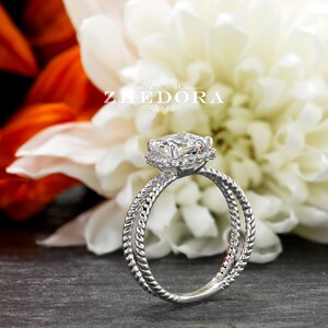 May include: A silver engagement ring with a large, round, clear diamond center stone surrounded by a halo of smaller diamonds. The band is twisted and has a rope-like design.