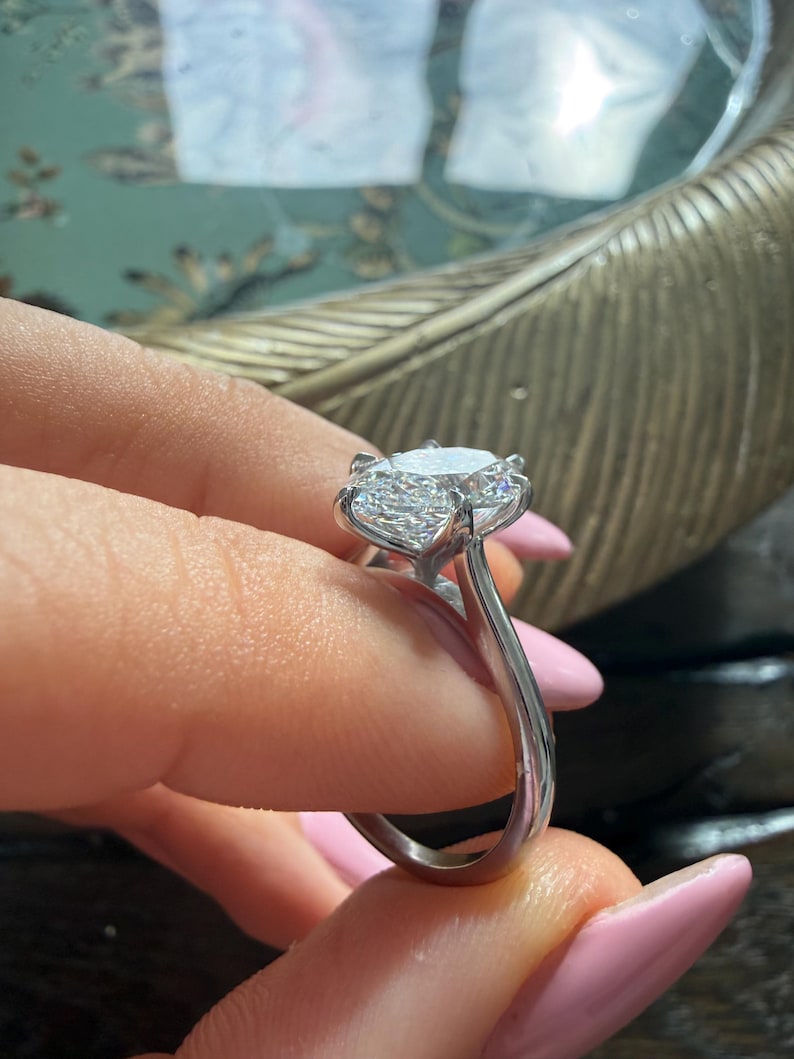 Pu&ograve; includere: Un anello d'argento con un grande diamante rotondo e trasparente come elemento centrale. Il diamante &egrave; tenuto in posizione da pi&ugrave; griffe. La fascia dell'anello &egrave; liscia e lucida, riflettendo la luce. L'anello &egrave; tenuto dalle dita di una persona.