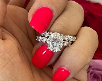 May include: A close-up of a silver engagement ring set with a large, round, clear center stone and a smaller band of sparkling stones. The ring is on a finger with bright red nail polish.