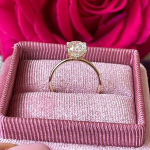May include: A gold engagement ring with a round, clear diamond in a pink velvet ring box.