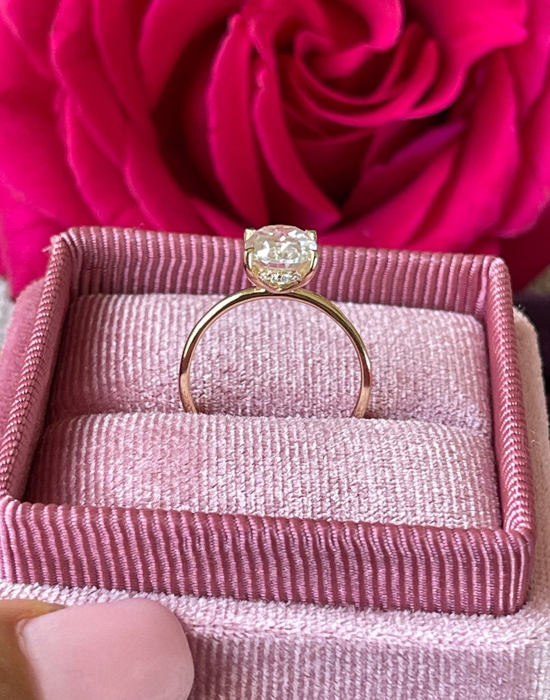 May include: A gold engagement ring with a round, clear diamond in a pink velvet ring box.