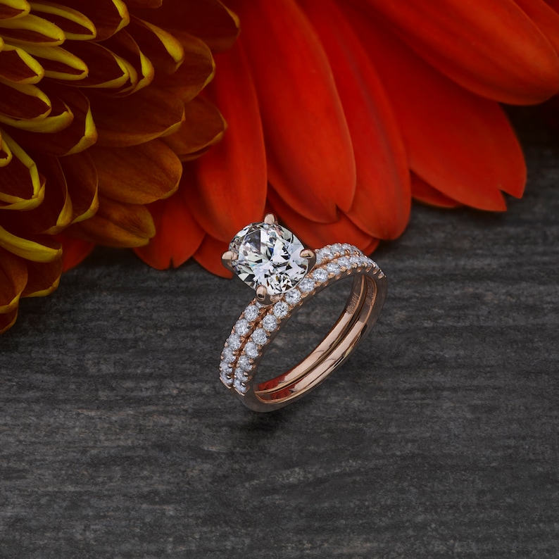 May include: A rose gold engagement ring set with a large oval-shaped center stone and a matching band with pave diamonds.