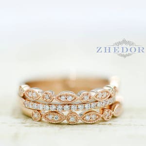 May include: Three rose gold rings with a delicate, vintage-inspired design. Each ring features a row of small, round diamonds set in a delicate, leaf-like pattern. The rings are stacked on top of each other, creating a beautiful and elegant look.