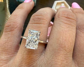 Può includere: Primo piano di una mano che indossa un anello d'argento con un grande diamante rettangolare trasparente. Il diamante è incastonato in una semplice montatura a griffe.