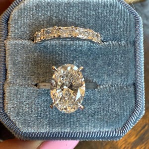 May include: Two diamond rings in a blue velvet ring box. The top ring features a band of rectangular diamonds. The bottom ring has a large oval-cut diamond set on a silver band.