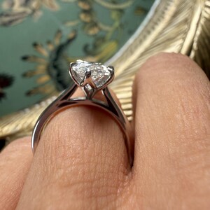 Pu&ograve; includere: Un anello di fidanzamento in argento con un grande diamante trasparente a taglio quadrato. L'anello ha una classica montatura a quattro griffe, che mette in risalto la brillantezza del diamante. La fascia &egrave; liscia e lucida. L'anello &egrave; su un dito.