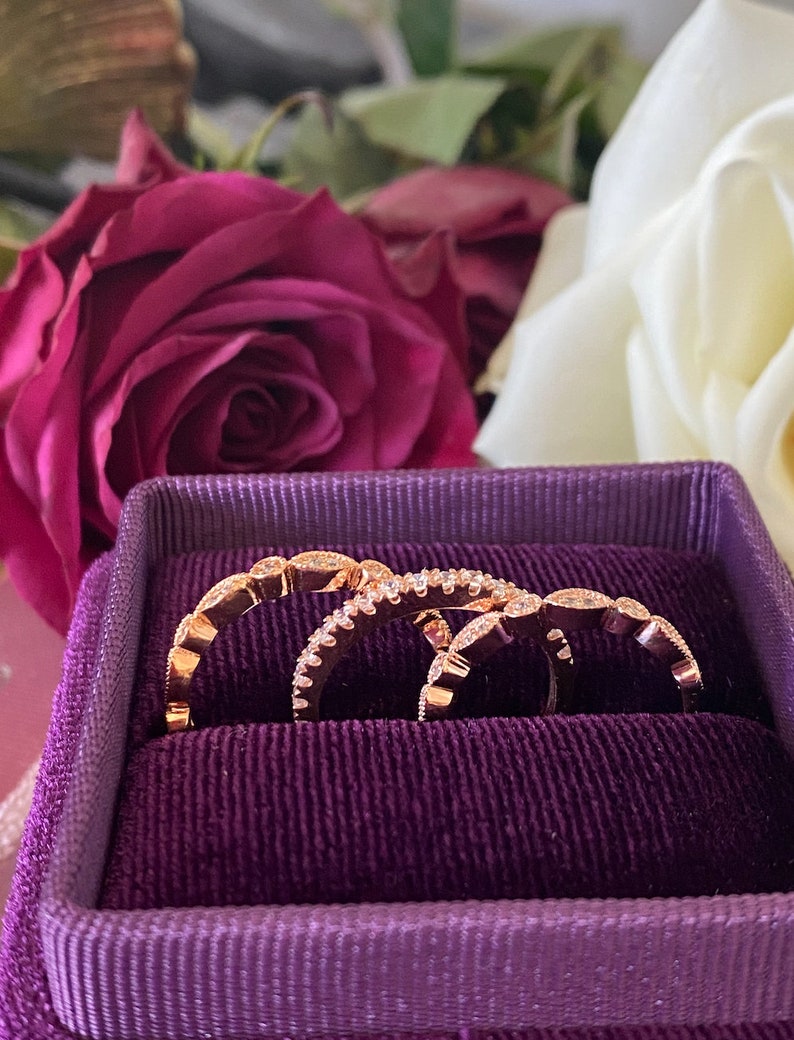 May include: Three rose gold rings with small diamonds set in a purple velvet ring box.