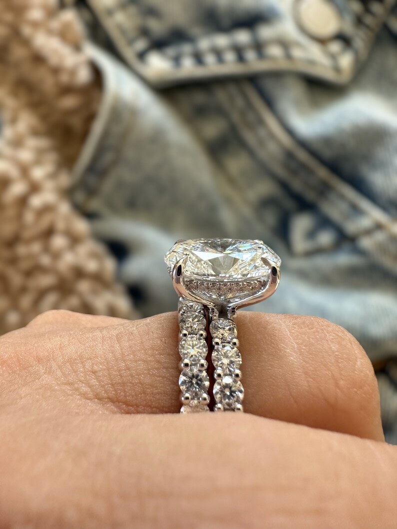 K&ouml;nnte beinhalten: Ein funkelnder Verlobungsring mit einem gro&szlig;en Diamanten im Kissenschliff. Der Ring ist in einem Platinband gefasst, mit einem passenden Eternity-Band. Die Diamanten funkeln brillant und zeigen das aufwendige Design und die Handwerkskunst.