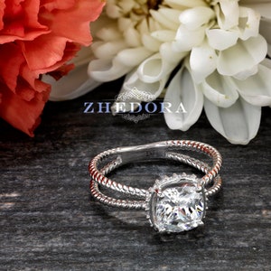May include: A silver ring with a square-shaped diamond set in a halo setting. The ring band is twisted and has a rope-like design.