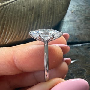 Pu&ograve; includere: Primo piano di un anello d'argento con una grande pietra preziosa trasparente a taglio ovale. L'anello ha una sottile fascia lucida e la gemma &egrave; tenuta in posizione da delicate griffe. Lo sfondo &egrave; sfocato, evidenziando i dettagli dell'anello.