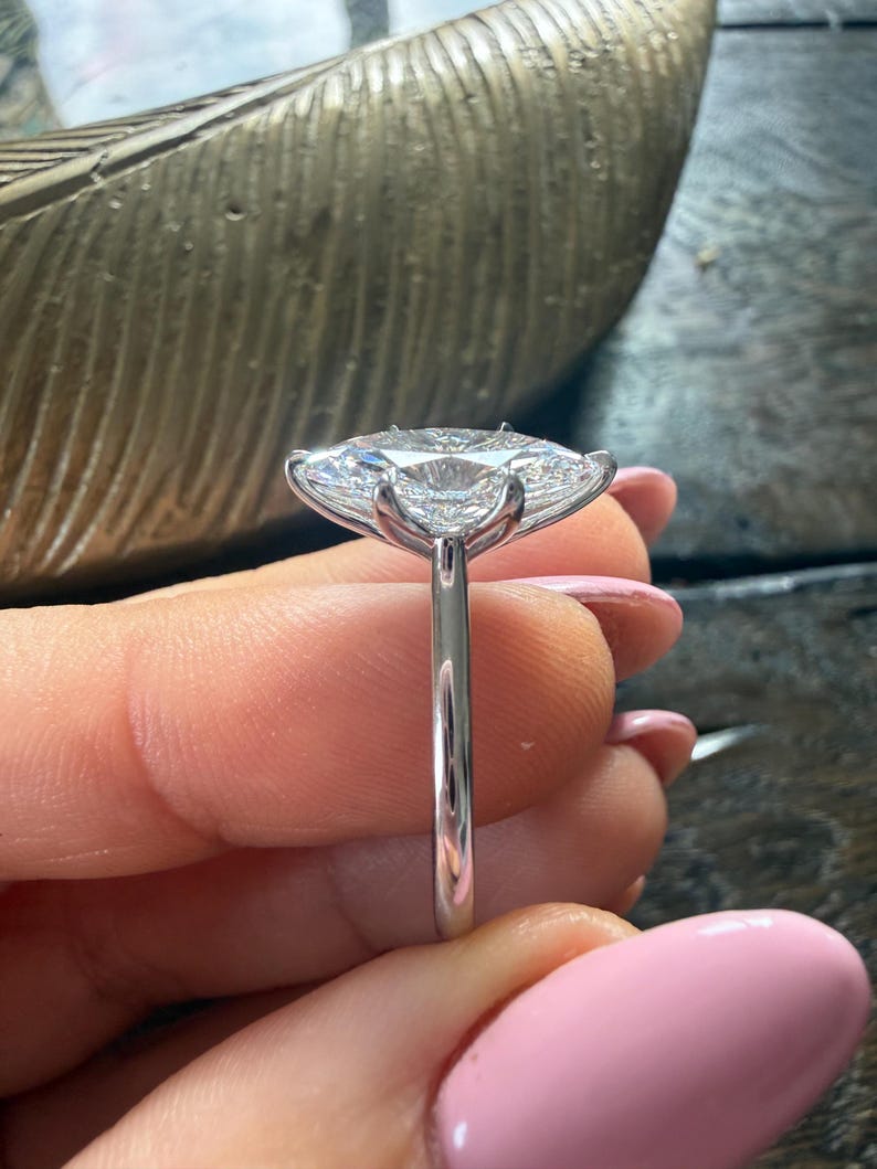 Pu&ograve; includere: Primo piano di un anello d'argento con una grande pietra preziosa trasparente a taglio ovale. L'anello ha una sottile fascia lucida e la gemma &egrave; tenuta in posizione da delicate griffe. Lo sfondo &egrave; sfocato, evidenziando i dettagli dell'anello.