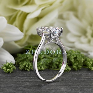 Puede incluir: Un anillo de compromiso de plata con un gran diamante ovalado transparente engastado en garras. El anillo tiene una banda sencilla.