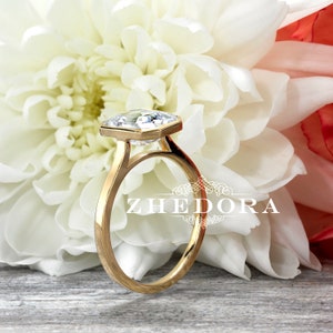 May include: A gold engagement ring with a large, clear, octagonal-shaped diamond. The ring is set on a white background with a white flower.