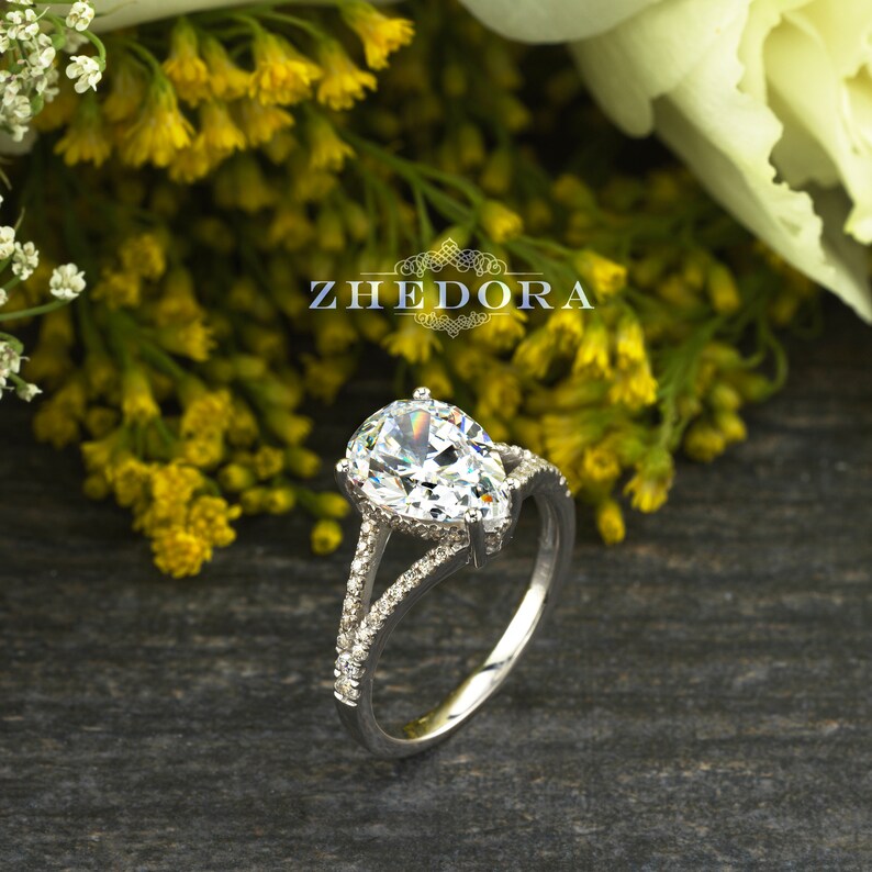 May include: A pear-shaped diamond engagement ring with a split shank and pave setting. The ring is set in white gold and features a large, sparkling diamond.