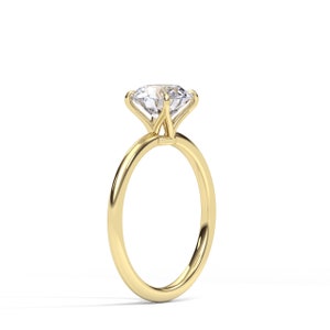 May include: A solitaire engagement ring with a large, clear diamond set in a four-prong setting. The band is a polished gold color, and the ring is displayed against a white background.