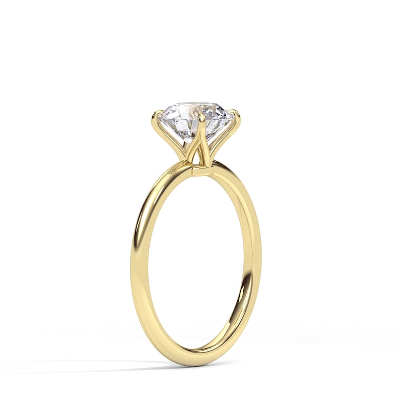May include: A solitaire engagement ring with a large, clear diamond set in a four-prong setting. The band is a polished gold color, and the ring is displayed against a white background.